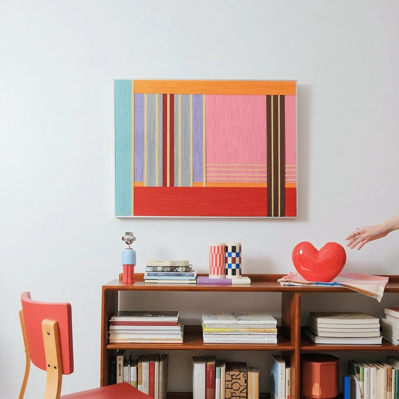 Rainbow Hearts wall art leaning on a tabletop beside a coffee cup, highlighting the bold red and pink stripe blocks and tight wool texture
