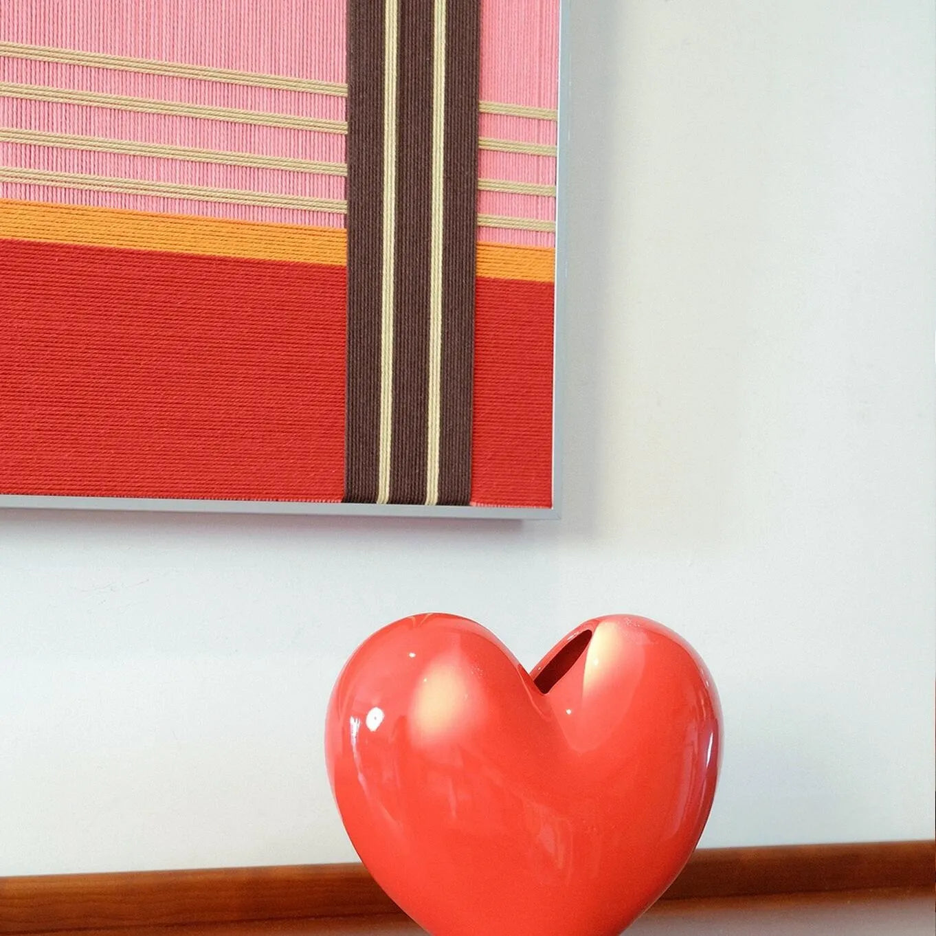 Close-up of Rainbow Hearts yarn wall art showing precise stitch detail and crisp color transitions between the red and pink stripe panels
