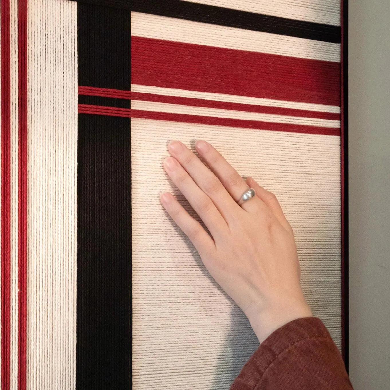 Close-up of Napoli RE002 textile art showing tactile wrapped yarn and the contrast between crimson red, cream, and black fibers.