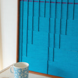 Close-up of Submersion RE018 textile art showing layered cerulean yarn, raised geometric lines, and its framed finish.