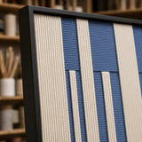 Angled close-up of Blue Cadence RE031 textile art showing its black frame and dimensional blue and ivory yarn texture.