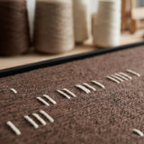 Angled detail of Cocoa Whispers textile art showing raised white yarn against a deep brown woven background.