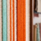Macro detail of Midtown Rhythm hand-woven textile art showing vertical fiber lines in vibrant orange, teal, blue, and cream.