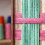 Detailed view of Pop Boulevard textured wall art featuring vertical teal yarn crossed by pink horizontal bands in a sleek metal frame.