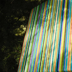 Reconstructing the Future yarn art panel displayed outdoors on a rock surface, emphasizing its bold multicolor stripe pattern against natural backdrop.
