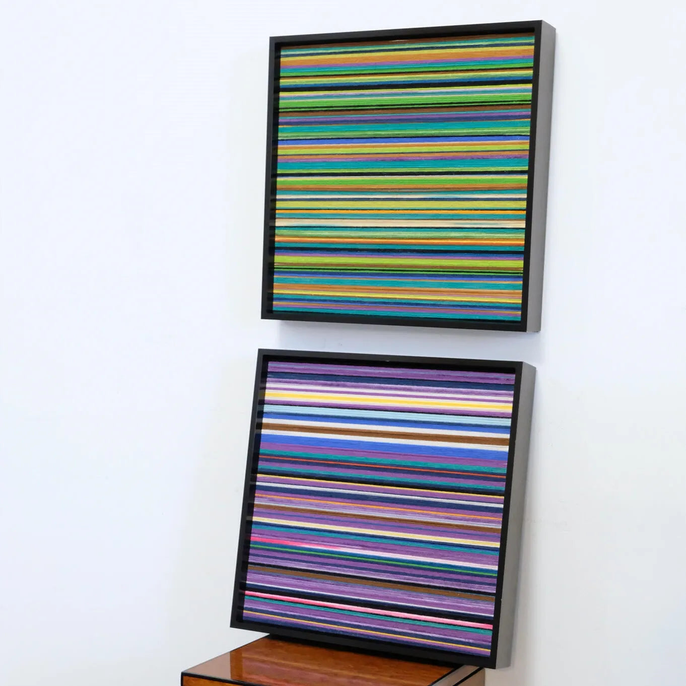 Two Reconstructing the Future yarn art panels stacked vertically on a white tabletop, highlighting their square format and seamless stripe alignment.
