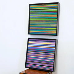 Two Reconstructing the Future yarn art panels stacked vertically on a white tabletop, highlighting their square format and seamless stripe alignment.
