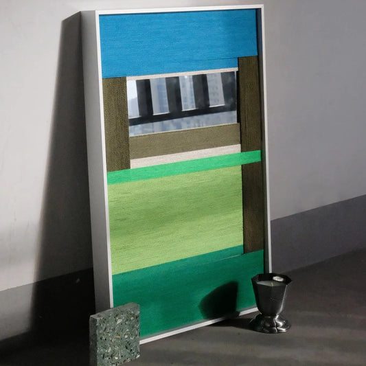 Riverside hand-woven wool yarn wall art with alternating sky-blue, slate grey, and forest green vertical panels and a neon-green accent stripe, displayed on a console table
