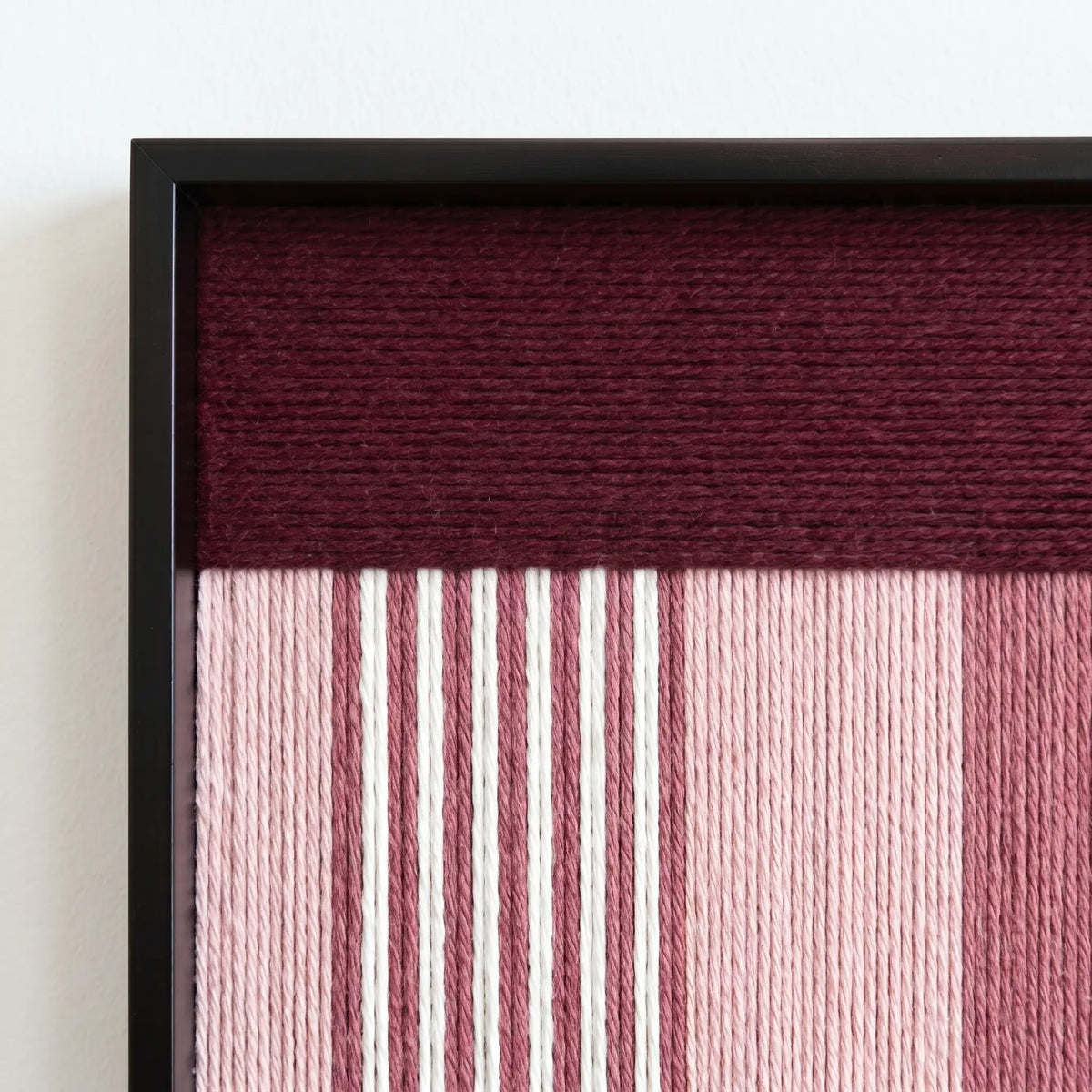 Macro shot of the black metal frame corner highlighting the professional craftsmanship and rich burgundy soft cotton cord fibers of the tapestry.