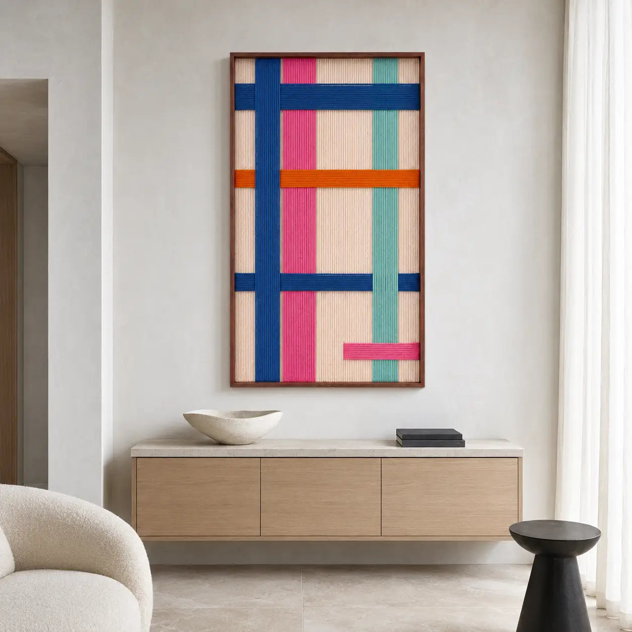 Clean entryway setting highlighting the vertical framed wool wall art hanging above a modern low wooden credenza in a bright room.