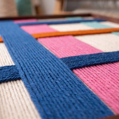 Close-up studio macro view of the hand-woven wool tapestry emphasizing textured blue yarn intersections over cream wool foundations.