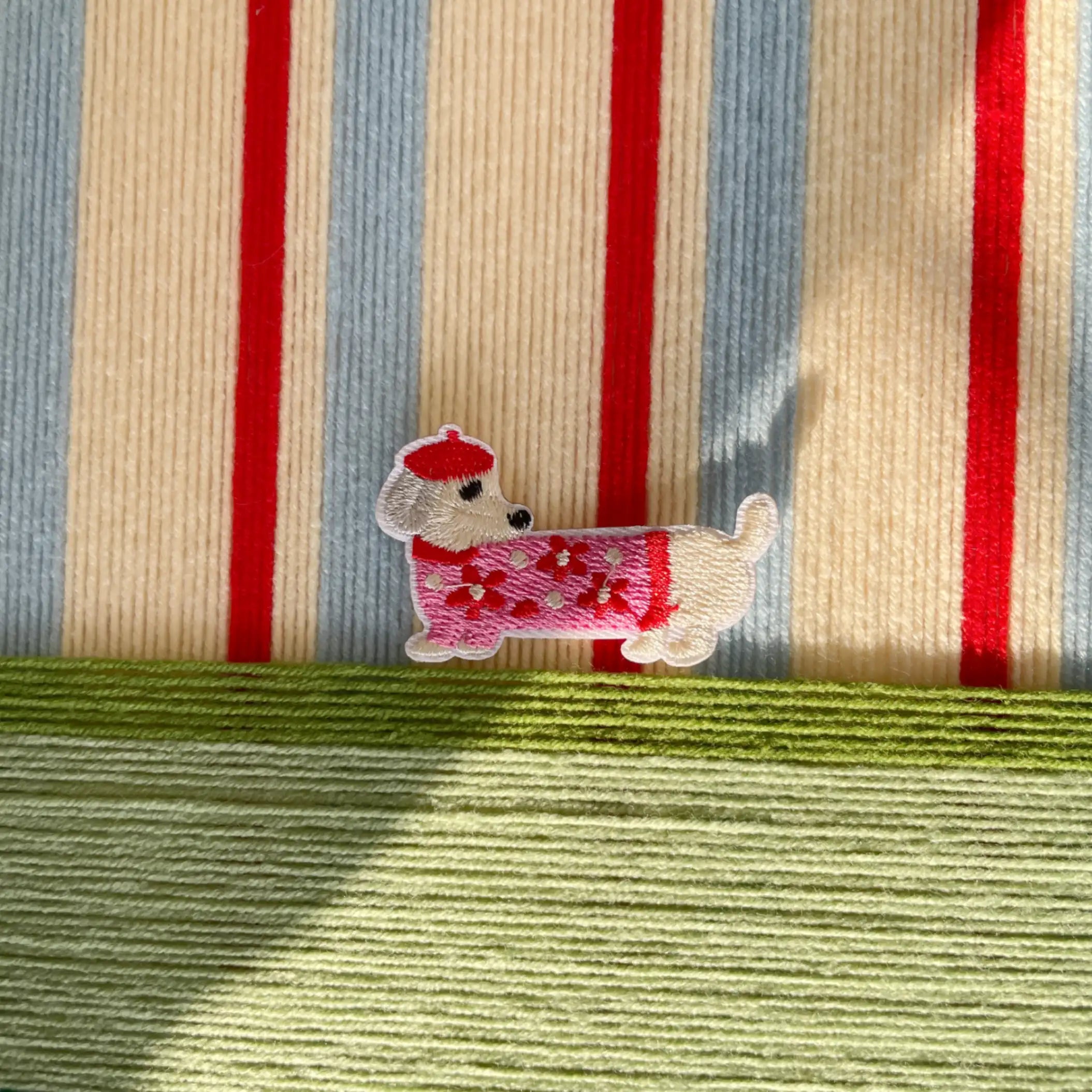 Macro shot of the hand-woven wool texture showing the raised scarlet stripes and the whimsical embroidered dog character detail.