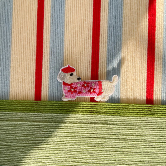 Macro shot of the hand-woven wool texture showing the raised scarlet stripes and the whimsical embroidered dog character detail.
