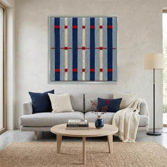 Modern hand-woven wool wall hanging styled in a bright living room above a grey sofa with navy blue accent pillows.