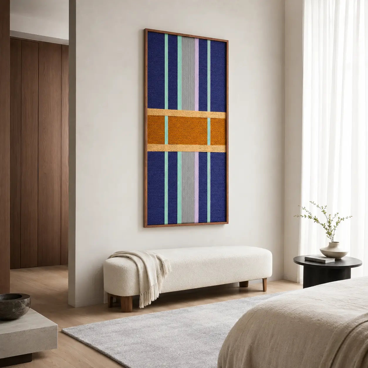 Clean modern bedroom interior featuring the vertical hand-woven wool tapestry displayed centrally above a neutral bench.