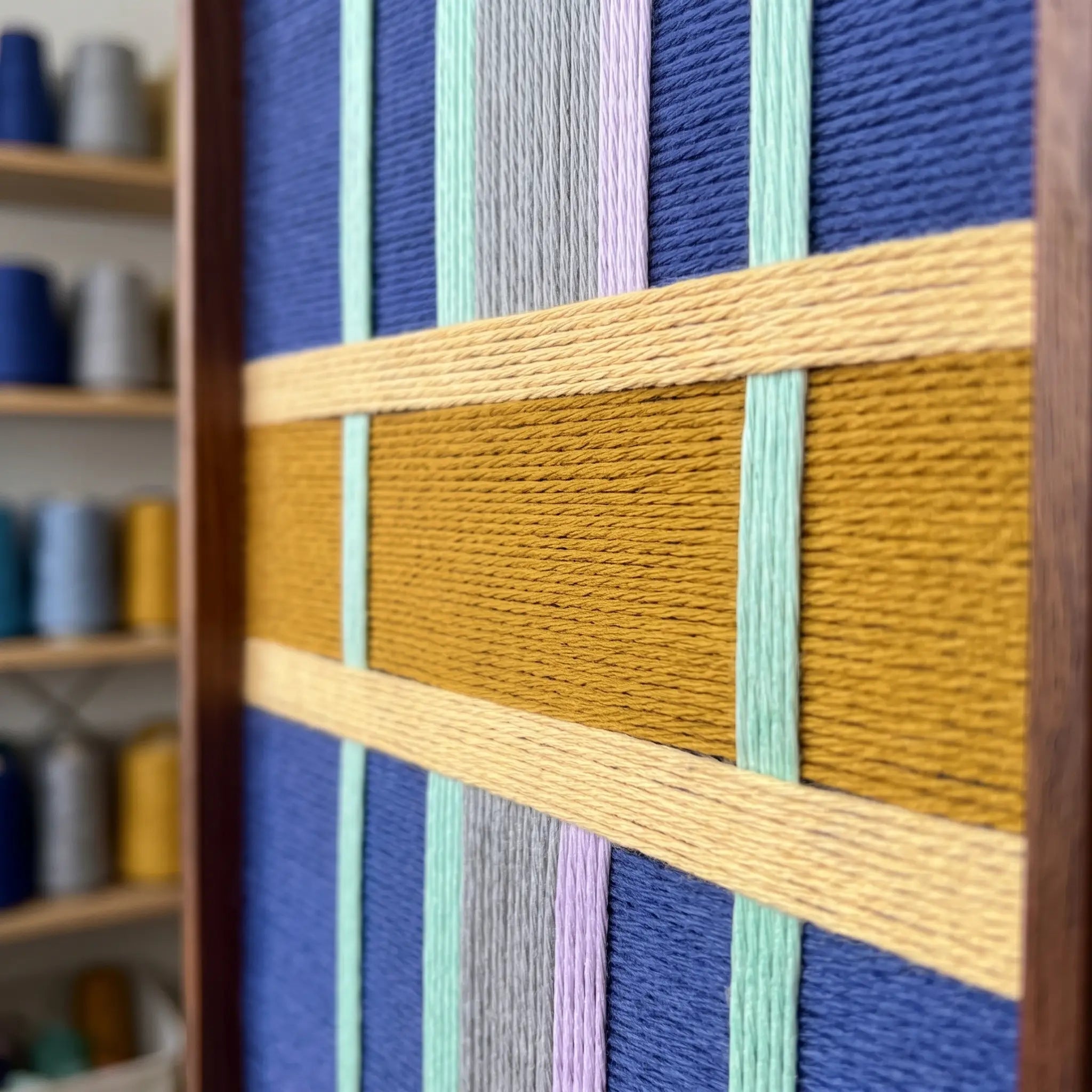 Detailed corner view of the hand-woven wool tapestry highlighting textured mustard yellow horizontal bands crossing vertical yarn fibers.