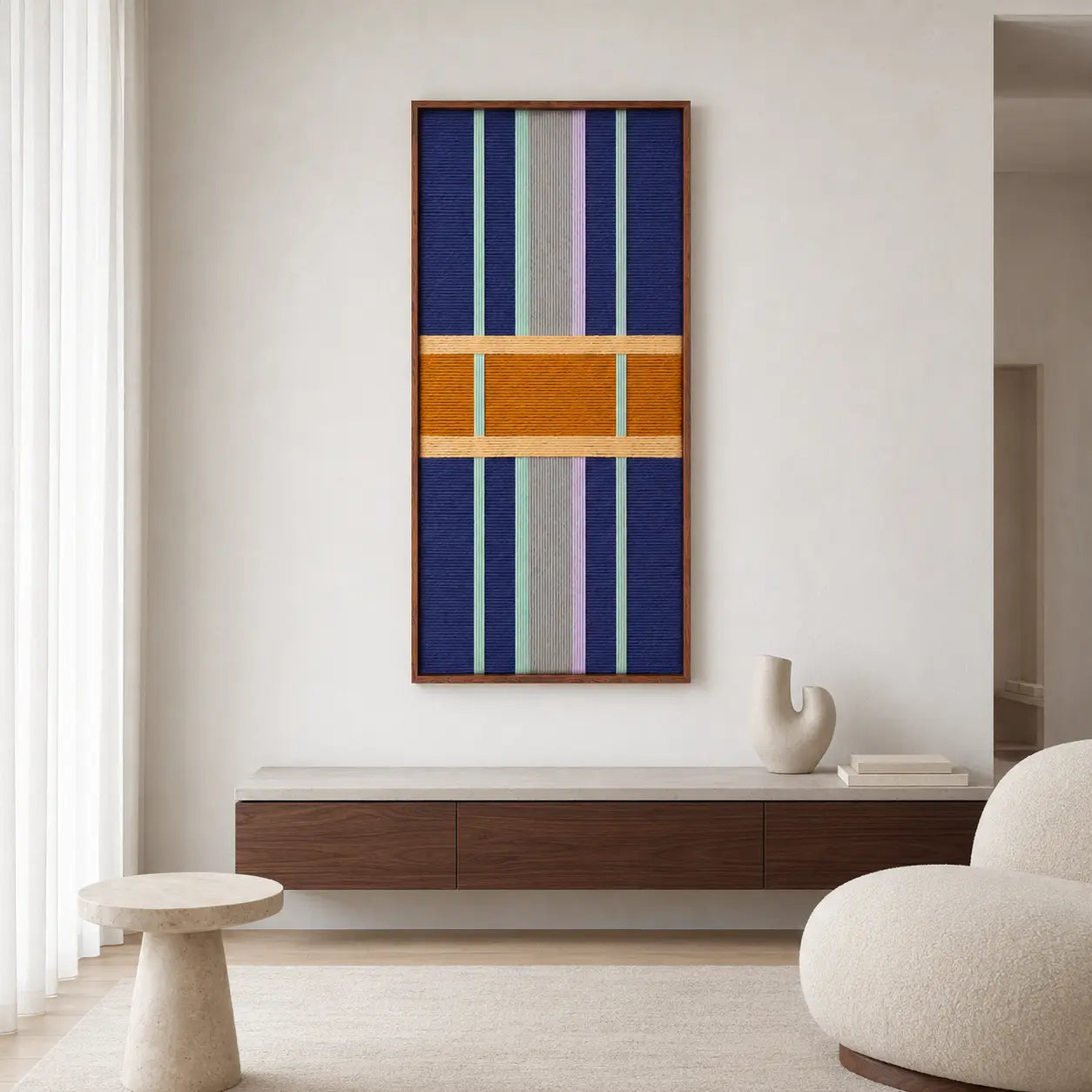 Cozy living room decor displaying the geometric framed wool tapestry hanging above a low wooden media console in a bright space.