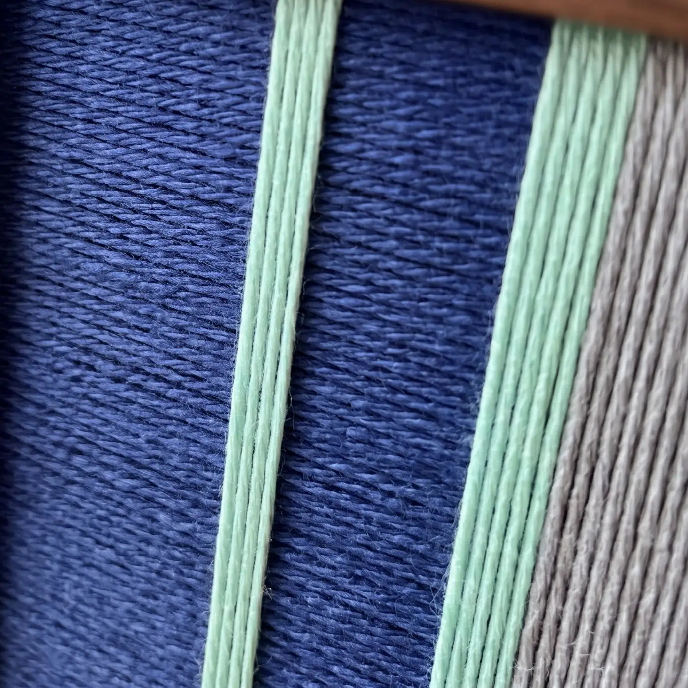 Close-up macro detail of the hand-woven wool tapestry showing textured vertical navy blue, mint green, and grey yarn structures.