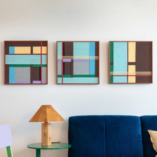 Close-up of the Sedona Red Thread triptych wall art hanging in a living room above a vibrant blue sofa and a unique geometric wooden lamp.