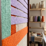 An angled close-up of the Sedona Twilight hand-woven wool tapestry showing vibrant orange, purple, and teal fiber art details.