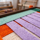 Macro close-up view of the Sedona Twilight hand-woven wool tapestry highlighting the colorful purple, orange, and cream yarn texture.