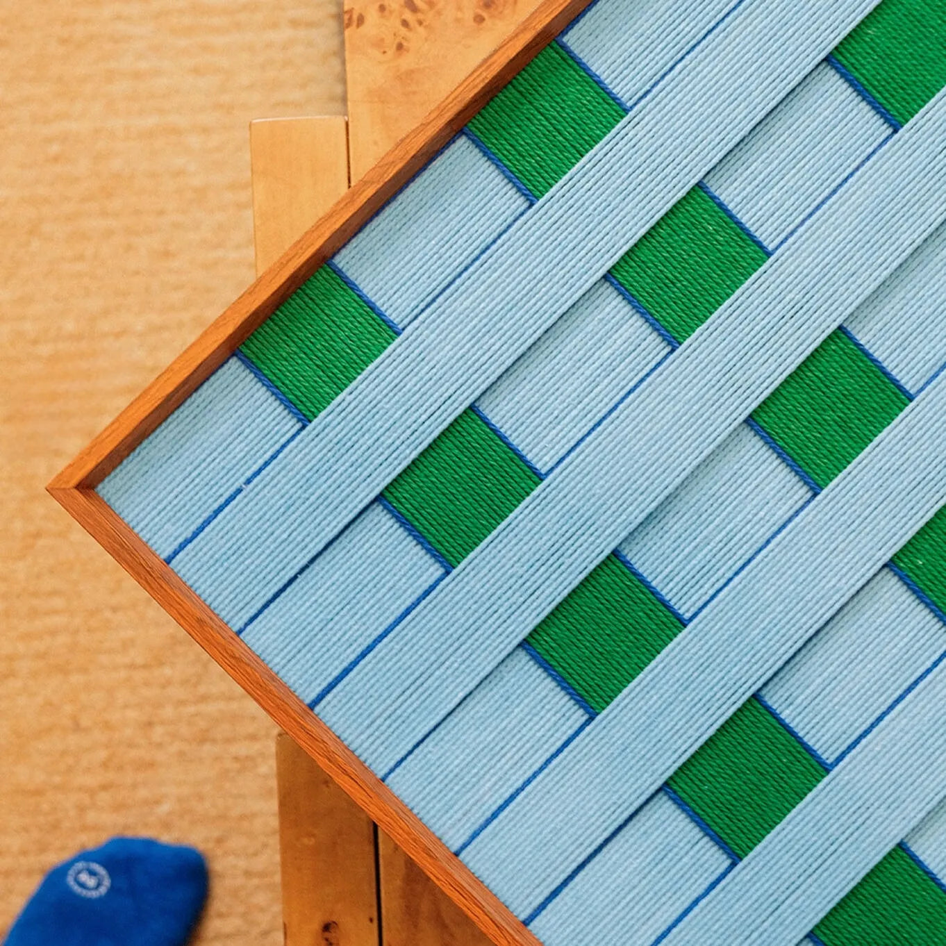 Seine Riverbank yarn wall art flat lay view on a wooden tabletop with yarn tools, emphasizing its uniform stripe width and square proportions
