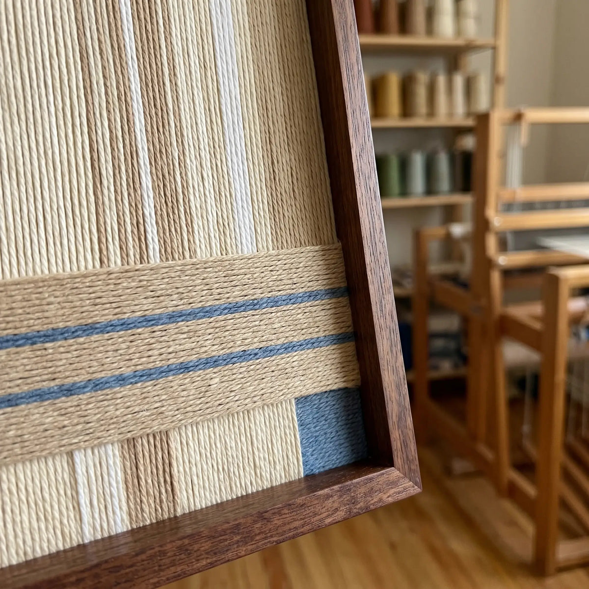 soft cotton cord fiber artwork shown from an angled perspective in a sunlit artist studio with a wooden weaving loom in the background.