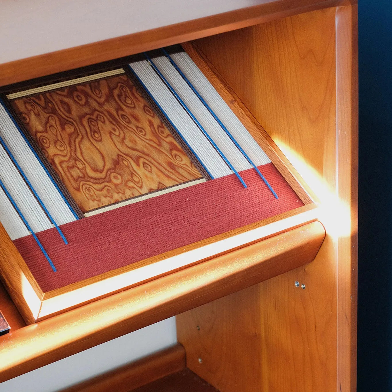 A unique perspective of the framed wool art placed inside a wooden shelf, showing the dimensional quality of the hand-woven fibers.
