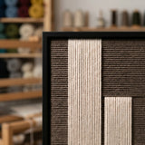 Close-up of the Silent Stelae framed wall art showing the precision of the hand-woven cream yarn set within a modern black frame.