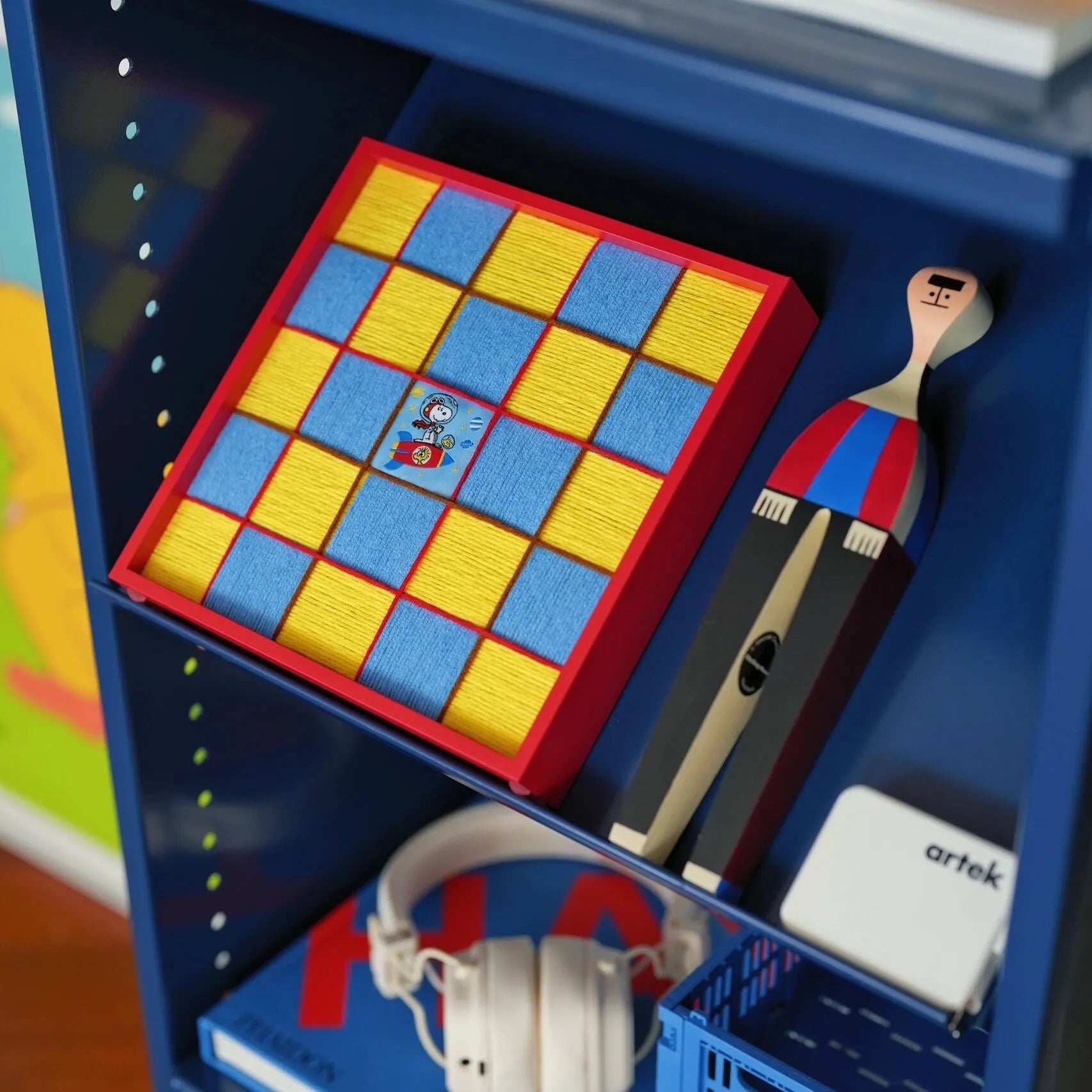 Styled shelf view featuring the hand-woven checkerboard art piece next to headphones and decor, showcasing its versatility in trendy home styling.