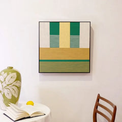 Spring Breeze Wheat Field yarn wall art hung on a wall above a chair, emphasizing its exact square proportions and clean geometric stripe design
