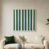 Square soft cotton cord wall art featuring vertical stripes in forest green, pale blue, and cream, hanging above a cream-colored sofa with green accent pillows.