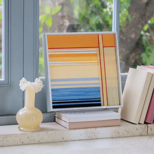 Love at Sunset framed yarn art displayed on a sunlit windowsill beside books and a ceramic vase