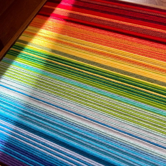 Close-up of Rainbow SQ004 hand-wrapped yarn transitioning through crimson red orange yellow green and blue bands