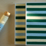 Horizontal and vertical Spring Lake SQ039 striped yarn artworks overlapping beside cream and blue yarn materials