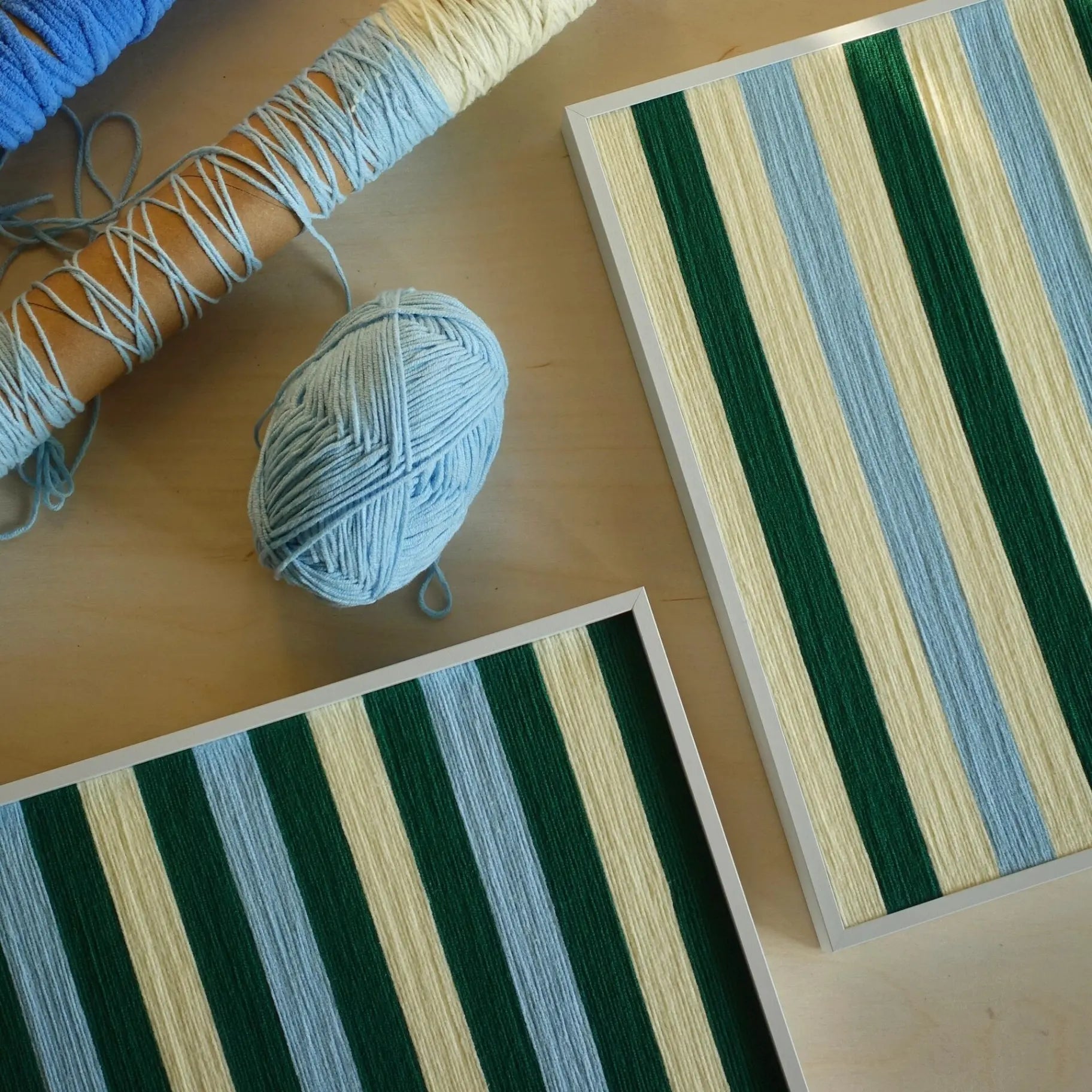 Overhead view of two Spring Lake SQ039 green blue and cream striped yarn artworks with a blue yarn ball and wrapped spools