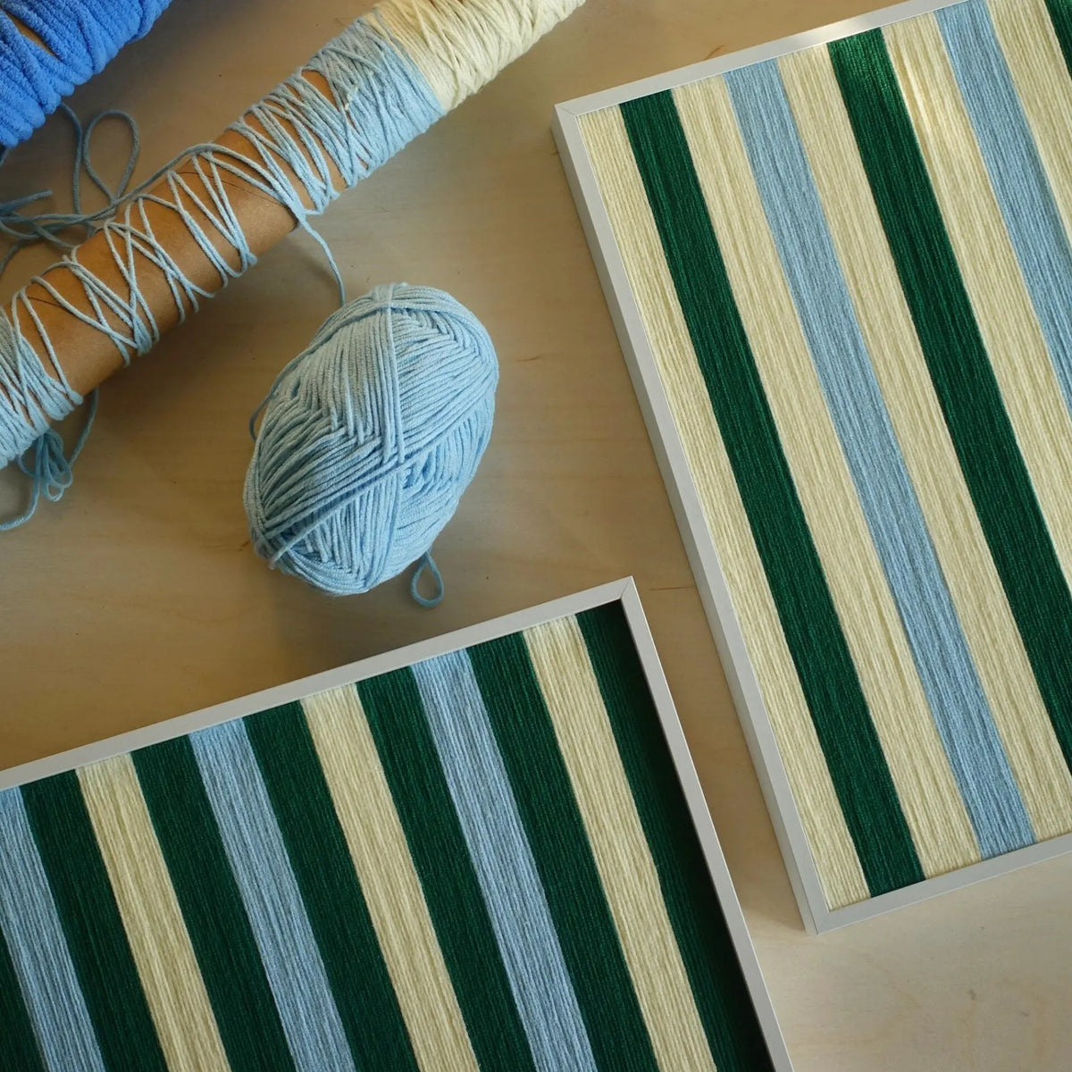 Overhead view of two Spring Lake SQ039 green blue and cream striped yarn artworks with a blue yarn ball and wrapped spools