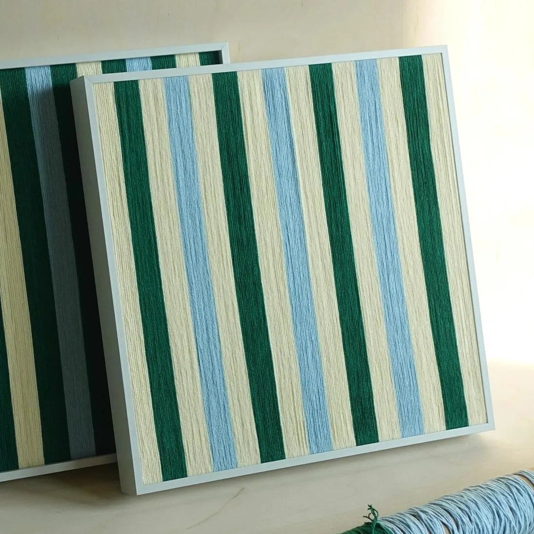 Two Spring Lake SQ039 green blue and cream striped framed yarn artworks shown together from the front in the studio