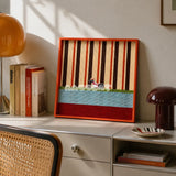 Tangerine Stripe Pup Venture SQ044 striped framed yarn art with a dog motif displayed on a desk beside books and a cane chair