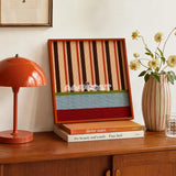 Tangerine Stripe Pup Venture SQ044 striped framed yarn art with a dog motif displayed beside an orange lamp and flowers on a wood cabinet