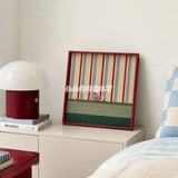 Scarlet Stripe Pup Saunter SQ045 striped framed yarn art with a dog motif displayed on a white bedside cabinet beside a red lamp