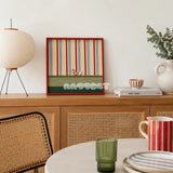 Scarlet Stripe Pup Saunter SQ045 striped framed yarn art with a dog motif displayed on a cane-front cabinet in a bright dining room