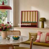 Coral Stripe Pup Wander SQ046 striped framed yarn art with a dog motif displayed above a green bench beside a round table in a bright dining nook