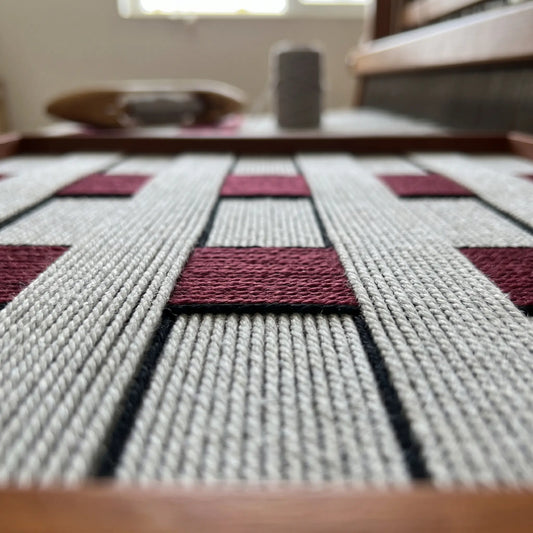 Macro view of Ruby Lattice SQ106 showing gray and deep red hand-wrapped yarn in a checkerboard pattern.