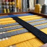 Angled workshop view of Golden Monsoon SQ110 highlighting dimensional black, yellow, and blue yarn craftsmanship.