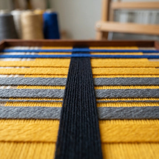 Macro view of Golden Monsoon SQ110 showing raised black yarn over yellow, gray, and cobalt blue bands.