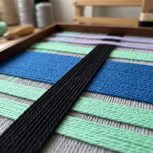 Angled macro view of Winter Aurora SQ112 showing raised black yarn over cobalt blue and mint green layers.