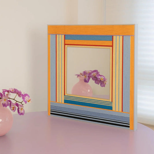 Angled view of Miami Sunsets SQ118 textile mirror on a pastel purple table reflecting a pink orchid.