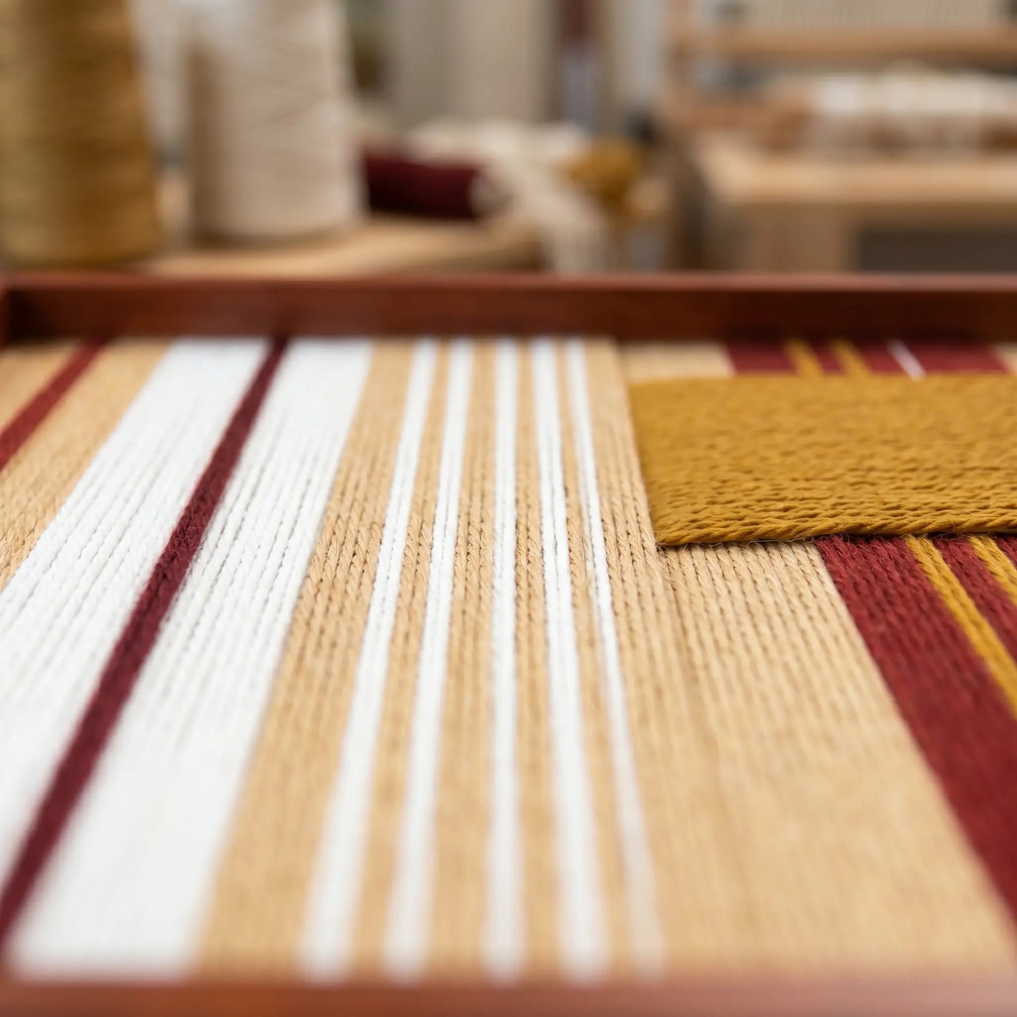 Low-angle close-up of Carmine Pulse SQ121 highlighting textured carmine red, mustard yellow, white, and beige yarn.