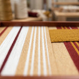 Low-angle close-up of Carmine Pulse SQ121 highlighting textured carmine red, mustard yellow, white, and beige yarn.